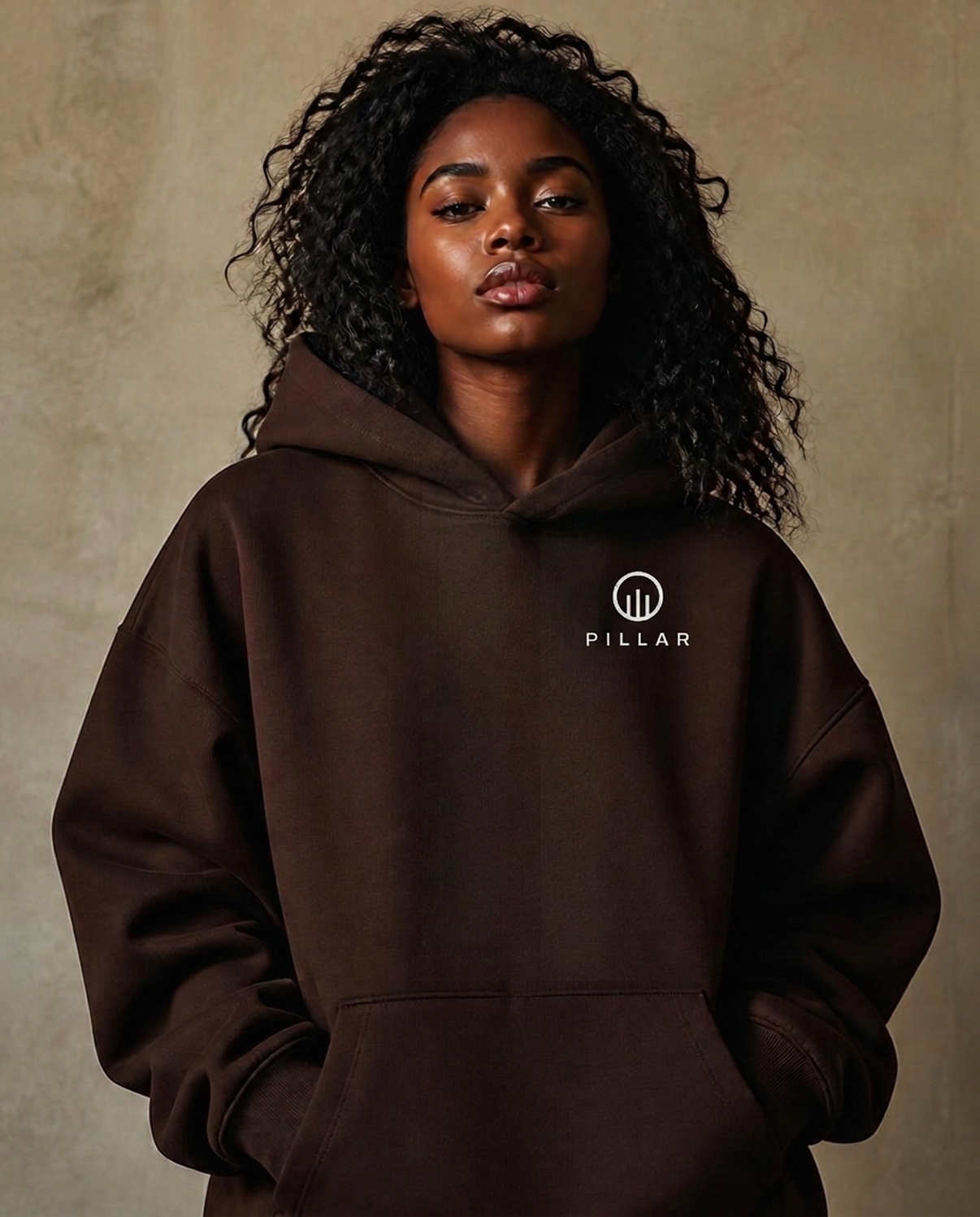 Black female model wearing the brown PILLAR Forged Hoodie with the embroidered left-chest lockup